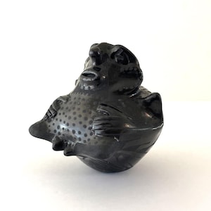 May include: A black ceramic frog figurine with a detailed, textured surface. The frog has a rounded body, detailed facial features, and small dots on its back. The figurine is a decorative item.