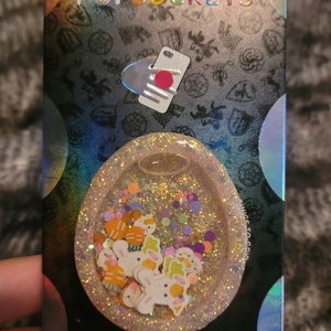 May include: A clear, round phone grip with a glittery background and colorful bunny and carrot charms. The grip is labeled "PopGrip" and "Game of Thrones".