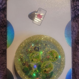 May include: A green and gold glitter phone grip with a PopSockets logo and the text "PopGrip".