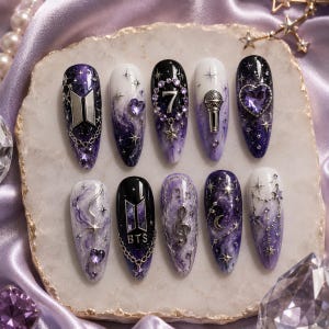May include: A set of ten press-on nails featuring a galaxy-inspired theme with shades of purple, black, and white. The designs include the BTS logo, the number 7, a microphone, a treble clef, a crescent moon, stars, and purple heart-shaped gems.