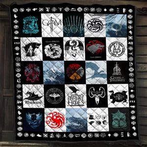 May include: A quilted throw blanket featuring a grid of twenty-five squares, each displaying various Game of Thrones themed graphics, logos, and text including Dracarys, Khaleesi, and Crows Before Hoes, all framed by a black border with white icons.