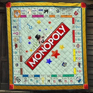 May include: A quilted blanket featuring a Monopoly board game design with a light green center, a large red diagonal Monopoly logo, and the iconic character in a top hat. The border includes various property names, game spaces, and yellow edges.