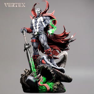 May include: A detailed statue of Spawn, a comic book character, standing on a grotesque base. The figure is predominantly gray and black, with a red cape and accents. He holds a large sword with green energy and has a chain around his waist. The word "VERTEX" is in the top left corner.