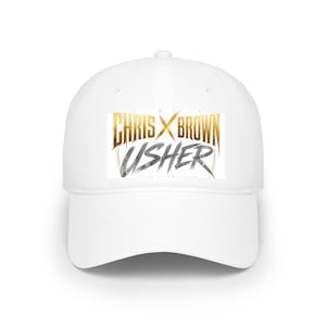 May include: White baseball cap featuring the text "CHRIS X BROWN USHER" in gold and gray. The cap has a curved brim and a structured crown. A stylish accessory for music fans.