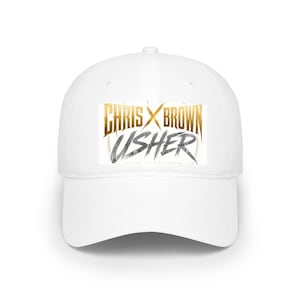 May include: A white baseball cap featuring a rectangular graphic on the front. The graphic displays the text CHRIS BROWN in a metallic gold font with an X symbol in the center, and the name USHER in a distressed, dark grey brushstroke font.