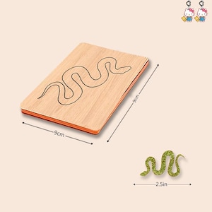 May include: A rectangular wooden board with a snake outline, measuring 9cm by 9cm, accompanied by a separate green glittery snake cutout measuring 2.5 inches in width. Two small Hello Kitty character charms are visible in the top right corner.