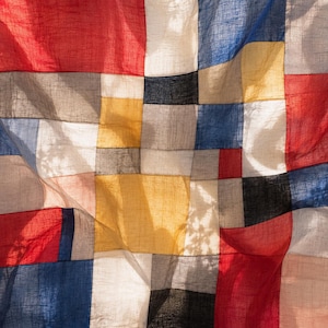 Könnte beinhalten: Ein Patchwork-Textil mit einem lebendigen Farbspektrum, darunter Rot, Blau, Gelb und Schwarz. Der Stoff ist in einem Rastermuster angeordnet, wodurch ein geometrisches Design entsteht. Das Textil wirkt leicht und fließend.