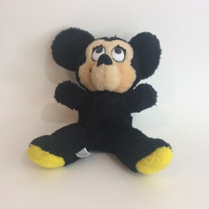 Puede incluir: Juguete de peluche Mickey Mouse negro con pies amarillos. El juguete tiene ojos grandes y una nariz marr&oacute;n.