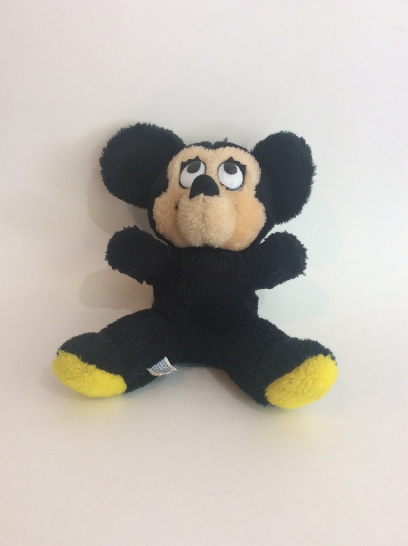 Puede incluir: Juguete de peluche Mickey Mouse negro con pies amarillos. El juguete tiene ojos grandes y una nariz marr&oacute;n.