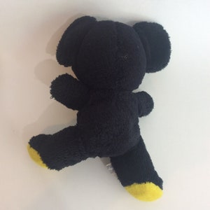 Puede incluir: Oso de peluche negro con pies amarillos. El oso est&aacute; de pie sobre una superficie blanca.