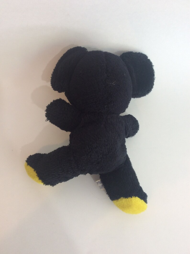 Puede incluir: Oso de peluche negro con pies amarillos. El oso est&aacute; de pie sobre una superficie blanca.