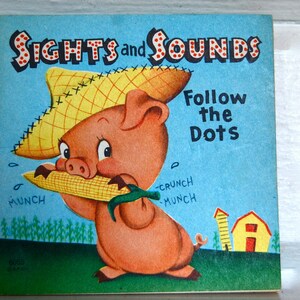 May include: A vintage children's book cover with a cartoon pig wearing a straw hat and eating corn. The book title is "SIGHTS and SOUNDS" and the subtitle is "Follow the Dots".