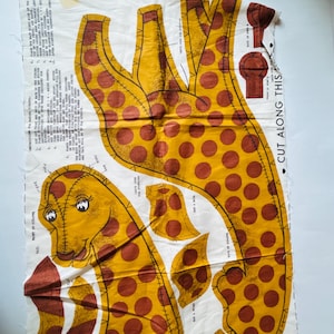 May include: A fabric panel featuring a giraffe pattern with yellow and brown spots. The giraffe's head, neck, and legs are visible, along with instructions and the text "CUT ALONG THIS". Ideal for crafting stuffed animals or decorative items.