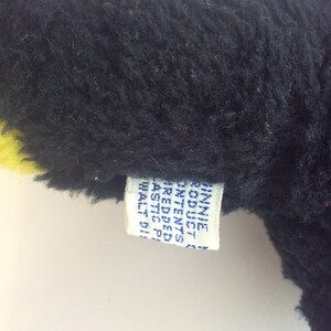 Puede incluir: Un juguete de peluche negro y amarillo con una etiqueta blanca que dice "ST. MICHAELS  MADE IN  CHINA  REG. NO.  PA 3282  ALL NEW  MATERIALS  SIZE 11"