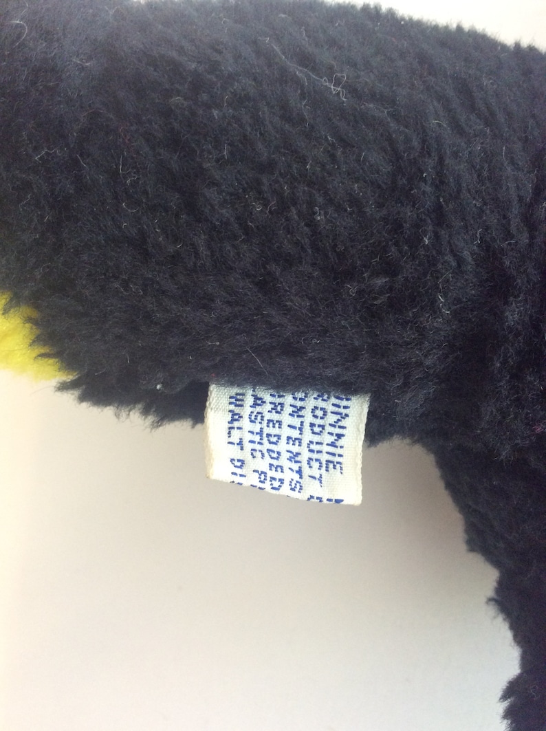 Puede incluir: Un juguete de peluche negro y amarillo con una etiqueta blanca que dice "ST. MICHAELS  MADE IN  CHINA  REG. NO.  PA 3282  ALL NEW  MATERIALS  SIZE 11"