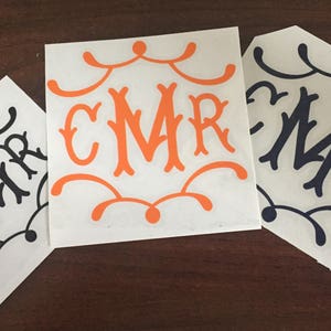 May include: Three white vinyl stickers with black and orange lettering. The stickers feature the letters CMR in a decorative font with a swirling design around the letters.