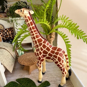 May include: A giraffe figurine with a cream-colored body and brown patches. The giraffe has a long neck, small ossicones on its head, and black hooves. It stands in a profile position, showcasing its spotted pattern and slender legs.