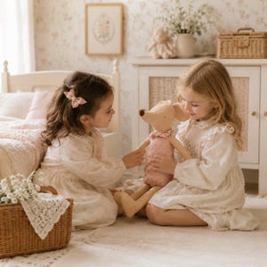 May include: A plush mouse toy with a tan body and a pink patterned romper featuring a small ruffled collar. The toy has long limbs, a brown nose, and stitched facial features, held by two children in a room with light-colored furniture and decor.