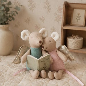 May include: Two plush mouse dolls with beige bodies and metallic gold wings. One mouse wears a teal outfit, the other a pink outfit. They sit together holding a small open book with the text A tiny seed printed on the cover, featuring a floral illustration.