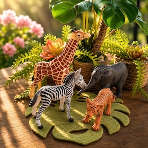 May include: A set of four animal figurines including a brown and tan giraffe, a black and white zebra, a grey elephant, and an orange and black tiger. The figures are arranged on a green felt leaf-shaped mat with textured surfaces.