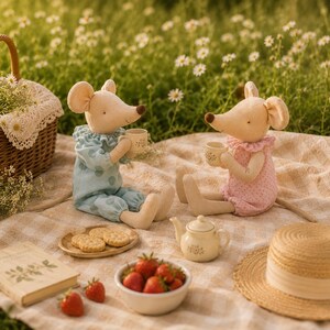 May include: Two plush mouse dolls sitting on a checkered blanket, one in a blue polka-dot outfit and one in a pink floral outfit, each holding a small ceramic teacup. A small ceramic teapot, a plate of round crackers, and fresh strawberries are nearby.
