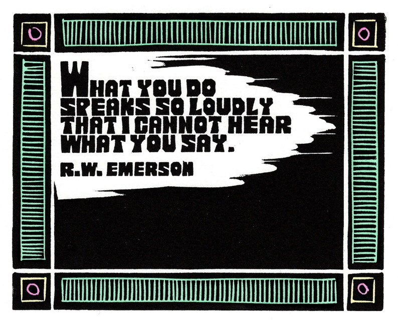 K&ouml;nnte beinhalten: Schwarz-wei&szlig; gerahmter Kunstdruck mit einem Zitat von R.W. Emerson: "WHAT YOU DO SPEAKS SO LOUDLY THAT I CANNOT HEAR WHAT YOU SAY." Der Text ist wei&szlig; auf schwarzem Hintergrund, mit einem dekorativen gr&uuml;nen und schwarzen Rahmen.