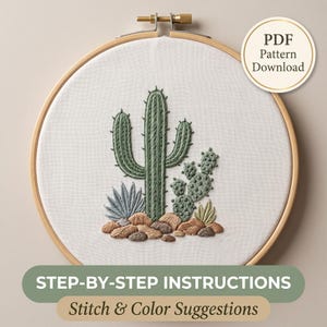 Op de afbeelding: Een ronde houten borduurring met witte stof en een geborduurd cactusontwerp. Het borduurwerk toont een hoge groene saguaro, een schijfcactus en kleinere vetplanten tussen bruine rotsen. De tekst luidt PDF Pattern Download.