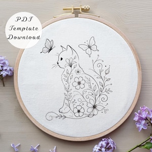 May include: An embroidery hoop with a cat design, adorned with flowers and butterflies. The cat is illustrated with floral patterns. The text "PDF Template Download" is in a white circle. The hoop is made of wood.