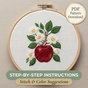 Puede incluir: Un bastidor de bordado redondo de madera con tela blanca que presenta un diseño bordado a mano de una manzana roja y flores de manzano blancas con hojas verdes. Una insignia circular dice PDF Pattern Download. El texto dice STEP-BY-STEP INSTRUCTIONS.
