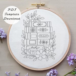 May include: A black and white embroidery hoop with a stack of books and floral design. The text "PDF Template Download" is in the upper left corner. The embroidery hoop is made of wood and has a gold-colored clasp.
