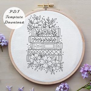 May include: A circular wooden embroidery hoop containing white fabric with a black line art pattern of a stack of four books decorated with various floral designs and leaves. The text PDF Template Download is visible in the upper left corner.