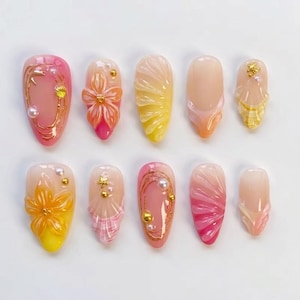 Peut inclure: Un ensemble de dix faux ongles avec divers motifs. Les ongles présentent des dégradés de couleurs, notamment rose, jaune et orange. Certains ongles ont des accents dorés, des perles et des motifs floraux ou en forme de coquillage.
