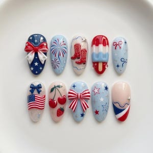 May include: A set of ten press-on nails featuring patriotic themes in red, white, and blue. Designs include 3D bows, fireworks, cowboy boots, a popsicle, the American flag, cherries, strawberries, and stars on various glossy base colors.