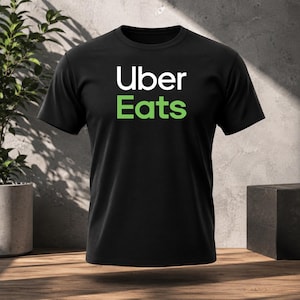 Può includere: Una t-shirt nera a maniche corte con la scritta Uber in bianco e Eats in verde stampata al centro del petto. Il capo presenta un girocollo e una vestibilità standard, realizzato in un tessuto nero a tinta unita con caratteri chiari.