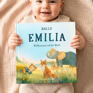 May include: A hardcover book with a light blue cover featuring the text "HALLO EMILIA Willkommen auf der Welt!" and an illustration of a baby, a fox, a leopard, and an elephant in a grassy field. The book cover has a matte finish and colorful art.