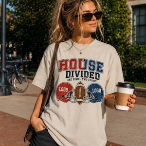 Peut inclure: Un t-shirt à manches courtes beige avec le texte HOUSE DIVIDED ONE HOME TWO TEAMS en rouge et bleu. Le motif comprend un casque de football américain rouge, un ballon de football et un casque bleu, chacun portant le mot LOGO imprimé.