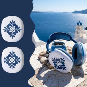 May include: Over-ear headphones featuring white ear cups with a dark blue floral pattern. The set includes two additional matching white and blue floral ear cup covers displayed separately on the left side of the image.