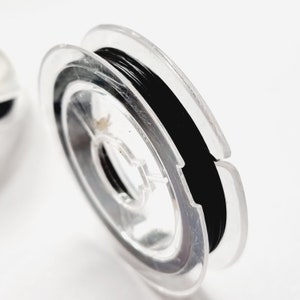 Może przedstawiać: Szpula czarnej gumki do włosów nawinięta na przezroczystą plastikową szpulkę.