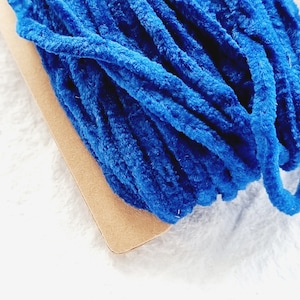 Op de afbeelding: Een close-up van een bundel felblauw, pluche garen, gewikkeld rond een stuk karton.