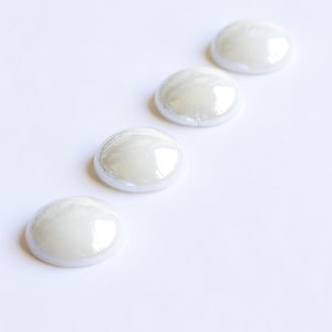 Könnte beinhalten: Vier weiße perlmuttartige Knöpfe mit glänzender Oberfläche.