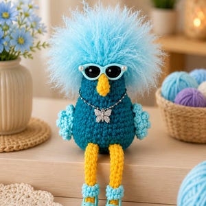 Puede incluir: Una muñeca de ganchillo con cuerpo azul verdoso oscuro, piernas amarillo brillante y un gran mechón de pelo azul claro esponjoso. La muñeca lleva gafas de sol azul claro, un collar de cadena plateada con un colgante de mariposa y sandalias de plataforma azul claro.
