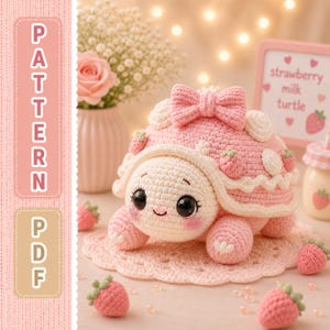 May include: A crocheted strawberry milk turtle with a pink shell, bow, and strawberry accents. The turtle has a cream-colored head and legs, and is sitting on a pink crocheted doily. The image also includes crocheted strawberries and the text "PATTERN PDF".