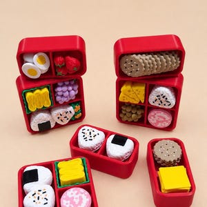 May include: A collection of five small red plastic bento boxes filled with miniature food erasers. The food items include various shapes of sushi, rice balls, crackers, cheese, fruit, and vegetables in vibrant colors like yellow, green, and pink.