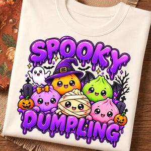Peut inclure: Un t-shirt couleur crème avec une impression graphique portant le texte SPOOKY DUMPLING en lettres violettes dégoulinantes. Le motif comprend des personnages de dessins animés mignons et souriants, des citrouilles et des pierres tombales.