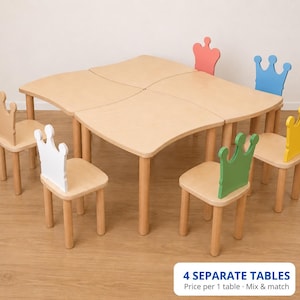 May include: A set of four light-colored wooden tables with curved edges that fit together to form a larger square surface, accompanied by five wooden chairs featuring backrests shaped like crowns in white, green, yellow, blue, and red.