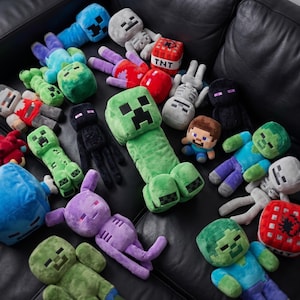 May include: A collection of Minecraft plush toys in various colors and designs, including a green Creeper, a blue zombie, and a gray skeleton. A red TNT block is also visible. The toys are arranged on a black surface.