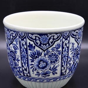 May include: A white ceramic planter with a blue and white floral design. The planter has a wide, round opening and a slightly flared base.