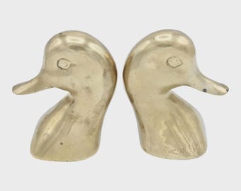 May include: A pair of brass duck head bookends. Each bookend features a detailed duck head with a curved neck and a prominent beak. The bookends have a polished, golden finish, adding a touch of vintage charm to any bookshelf.