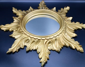 Puede incluir: Un espejo dorado y adornado con un diseño de estrella. El espejo tiene una superficie redonda y reflectante y un marco detallado e intrincado.