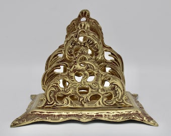 Op de afbeelding: Een gouden metalen brievenhouder met een sierlijk, ingewikkeld ontwerp. De houder heeft een vierkante basis en een hoge, open bovenkant.